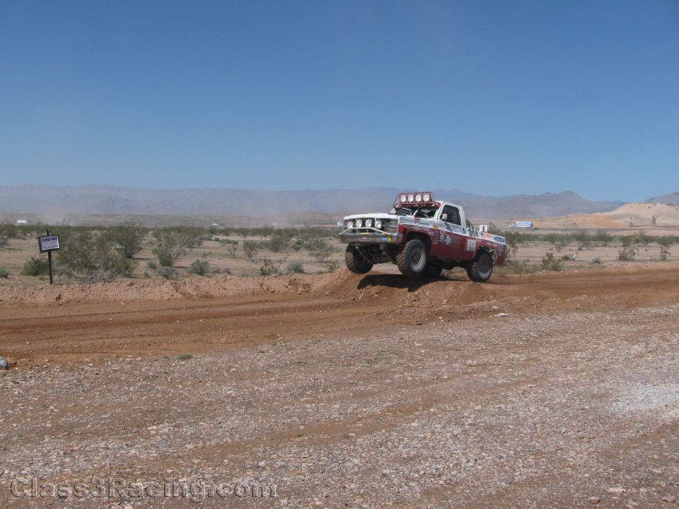 White and red off-road race truck cresting a desert berm