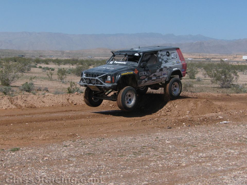 Gray camouflage SUV-bodied off-road race truck on a desert berm