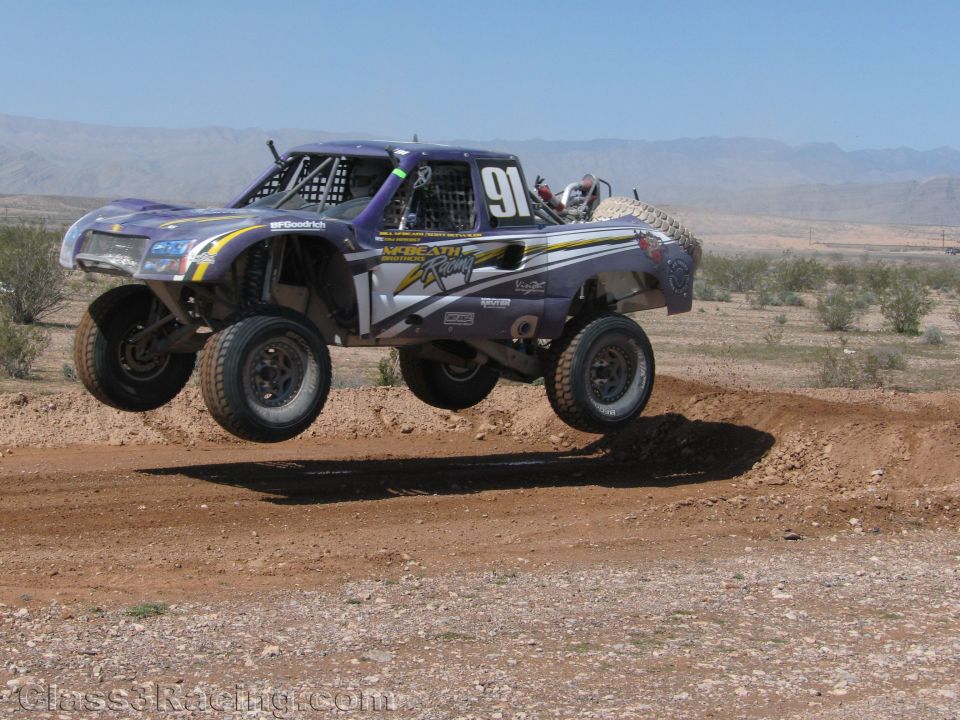 Purple No. 91 off-road race truck airborne over a desert jump