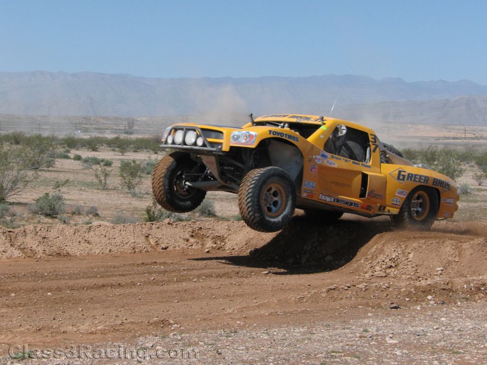 Yellow Green Bros off-road race truck airborne over a desert berm