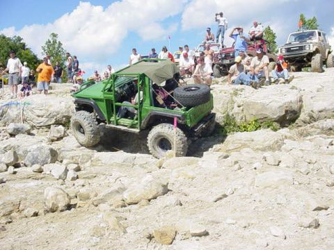 1992 Ford Bronco - Spectators watch as a modified green off-road vehicle navigates a challenging rocky incline.