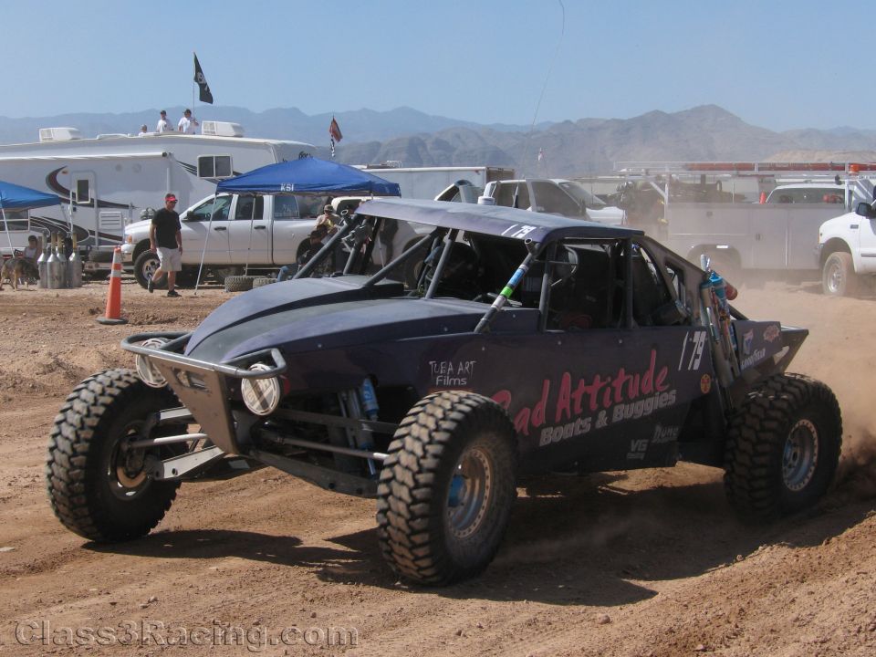 Dark off-road race buggy #79 turning on dirt track with mountains behind