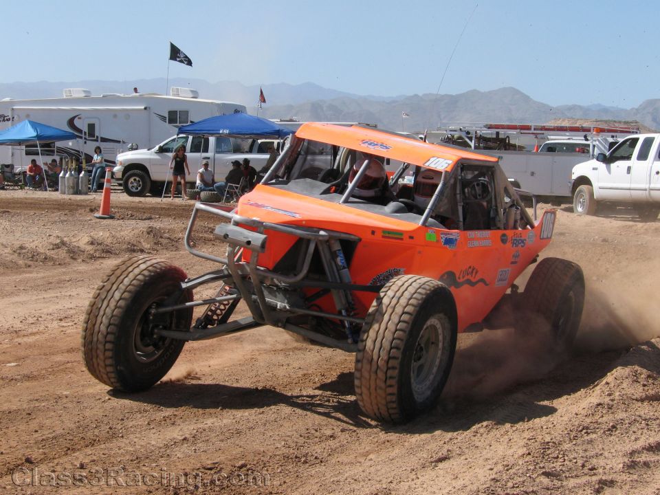 Orange single-seat off-road buggy cornering on dirt track