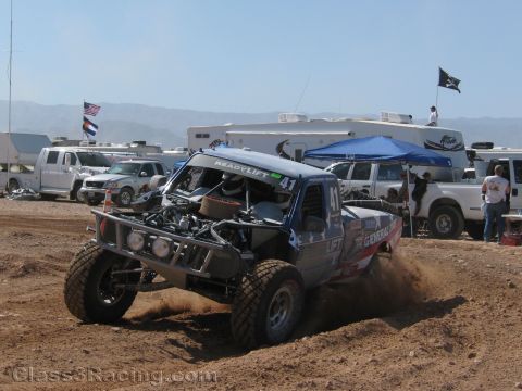 1990 Ford Bronco - dark off-road race truck numbered 41 with a ReadyLift windshield banner kicks up dust on a dirt course.