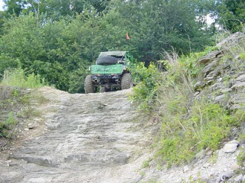 1992 Ford Bronco - A green off-road vehicle navigates a challenging rocky path surrounded by dense foliage.