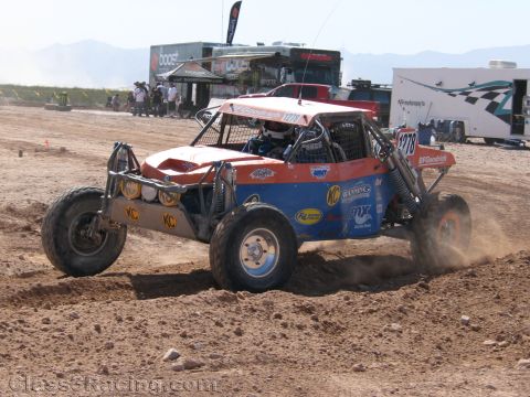 1990 Ford Bronco - orange, white and blue off-road race buggy numbered 1278 with KC lights races over a dirt course past pit trailers.