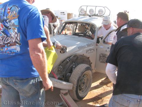 1990 Ford Bronco - Several people gather around a white VW Beetle race car in the pits, one holding a yellow fuel jug while others work on the front end.