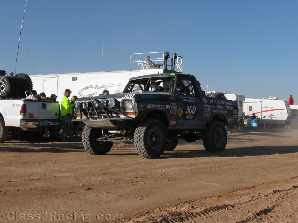 Black Ford Bronco off-road race truck number 300 staged in dirt pits