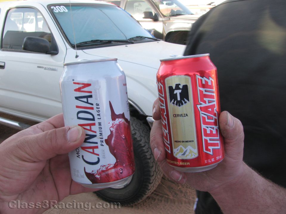 Two hands holding Molson Canadian and Tecate beer cans in front of a white truck