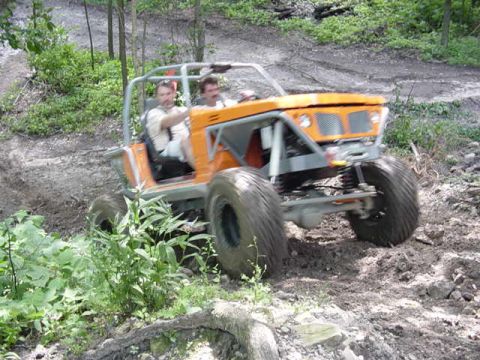 1992 Ford Bronco - Two people ride in an orange off-road buggy on a muddy, wooded trail.
