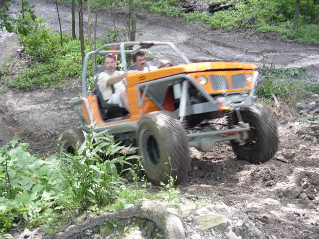 Orange off-road buggy with two occupants driving on a dirt trail