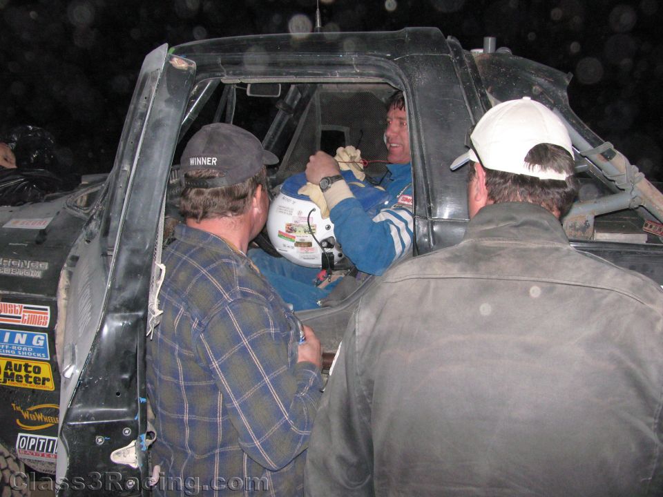 Crew members leaning into the cab of a black race truck talking to driver at night