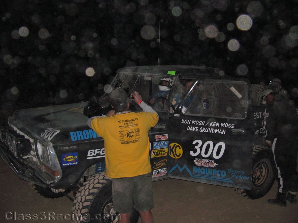 Crew working on dusty black Bronco race truck number 300 at night