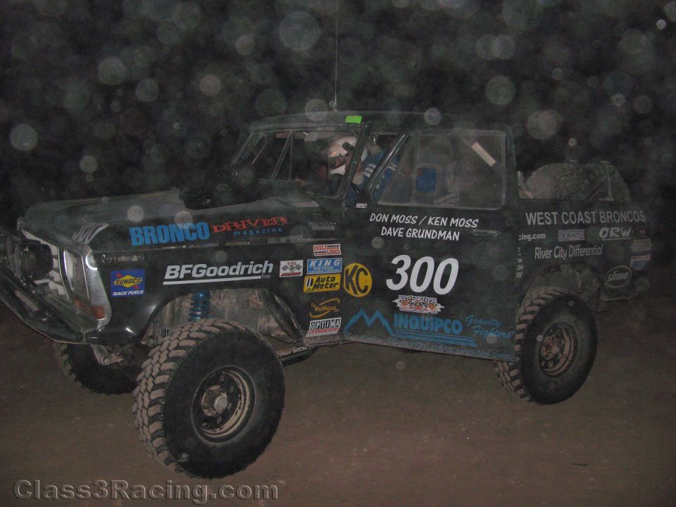 Side view of dusty black Ford Bronco race truck number 300 at night