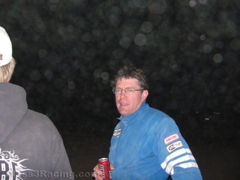 1990 Ford Bronco - man in a blue racing suit and glasses holds a soda can while talking with another person outdoors at night.