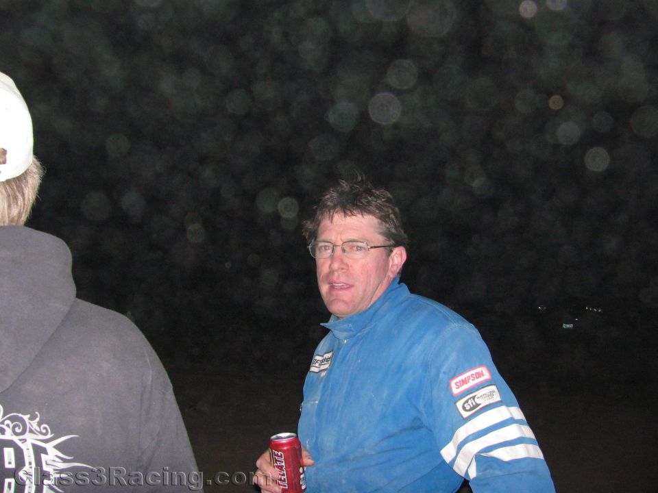 Man in blue racing suit and glasses holding a soda can talking outdoors at night