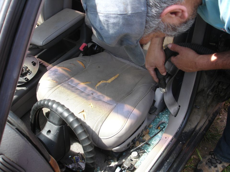 Car interior with gray seat, shattered glass on floor, person working inside