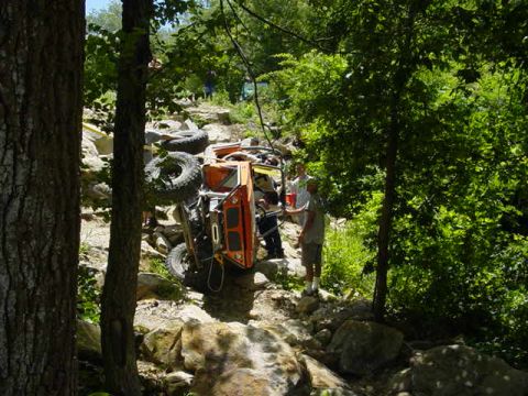 1992 Ford Bronco - An overturned orange off-road vehicle lies on its side amidst a rocky, wooded landscape.