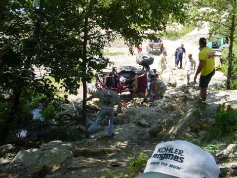 1992 Ford Bronco - An off-road vehicle is overturned on a rocky trail, with several people observing the scene.