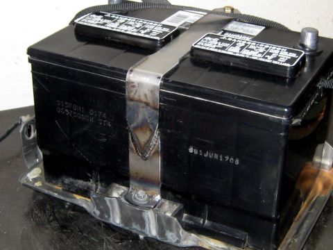 1996 Ford Bronco - A black Autolite car battery test-fitted in a fabricated bare-steel battery tray, held down by a welded hold-down strap running over the to…
