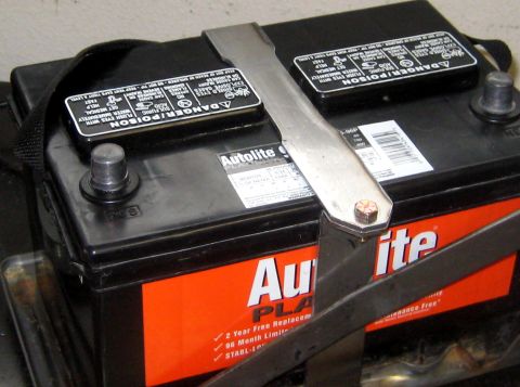 1996 Ford Bronco - A car battery is secured with a metal strap.