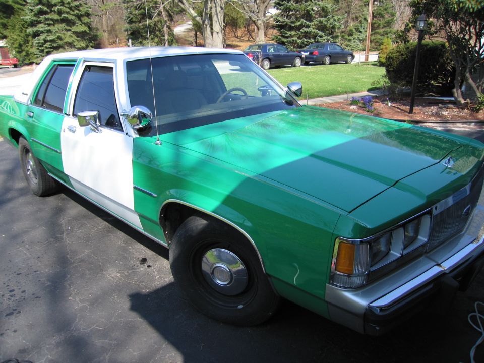Side view of green and white Ford sedan in driveway with houses behind