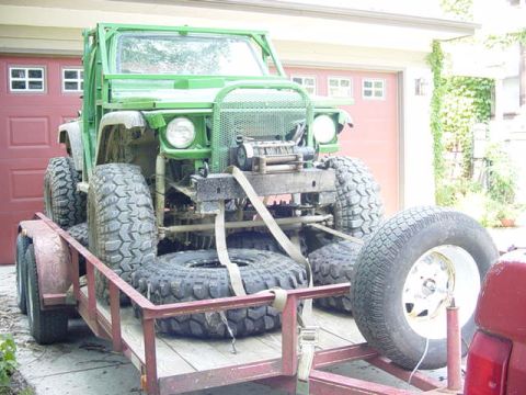 1992 Ford Bronco - Custom green off-road vehicle with oversized tires is loaded onto a trailer.