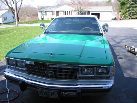 1991 Ford LTD Crown Victoria - Front view of a green Ford sedan with side spotlights, chrome grille and plate 351WP72, parked before a house and lawn.