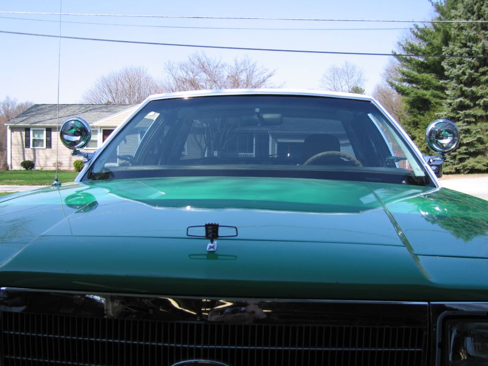 Hood and windshield of green sedan with two side-mounted spotlights