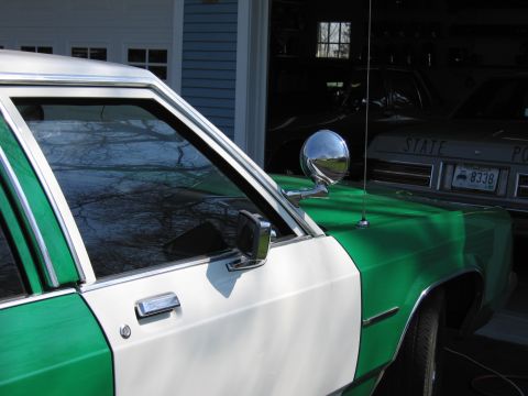 1991 Ford LTD Crown Victoria - Close view of the driver-side door, mirror and chrome spotlight of a green-and-white sedan parked near an open garage.