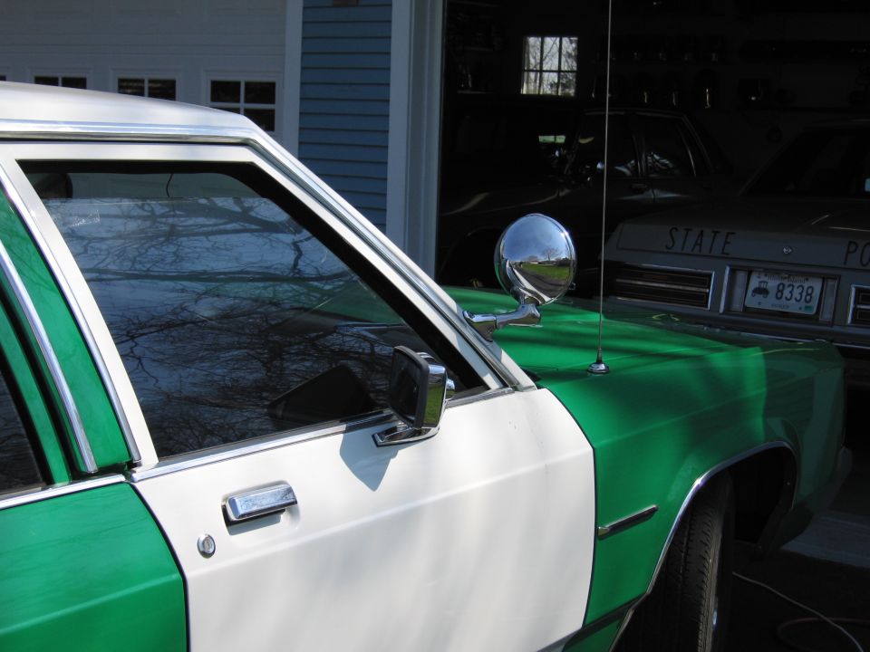 Driver door and chrome spotlight of green and white sedan near a garage