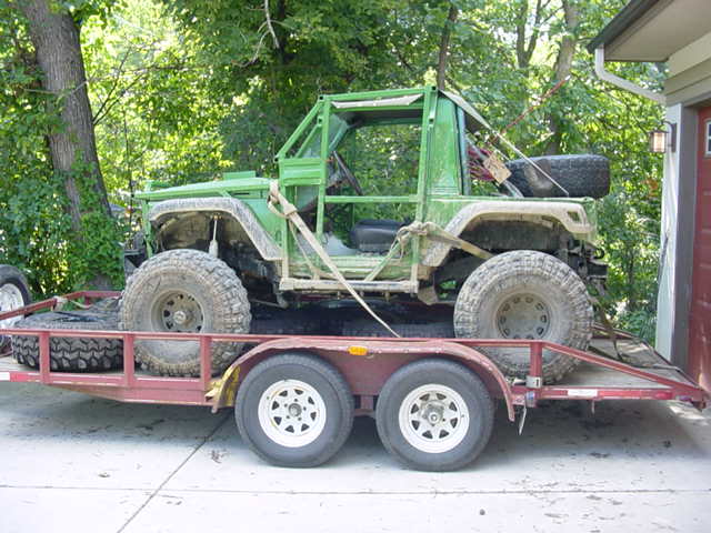 Green off-road vehicle with roll cage on a trailer. It has large tires and appears modified
