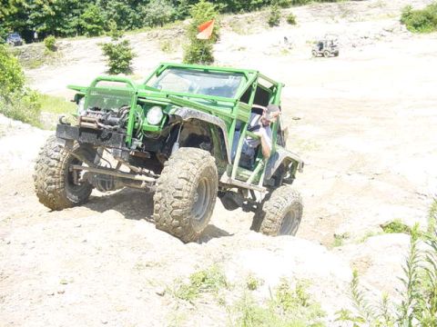 1992 Ford Bronco - A modified off-road vehicle navigates a challenging dirt terrain with a driver visible inside.