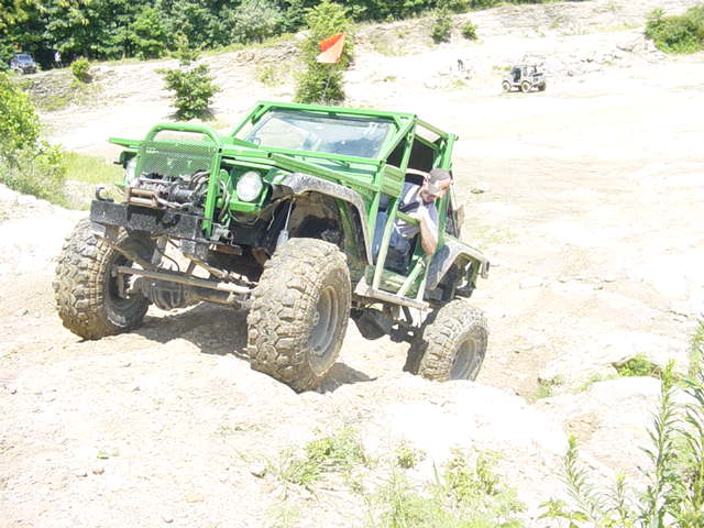 Green off-road vehicle with large tires and a roll cage, on a dirt track