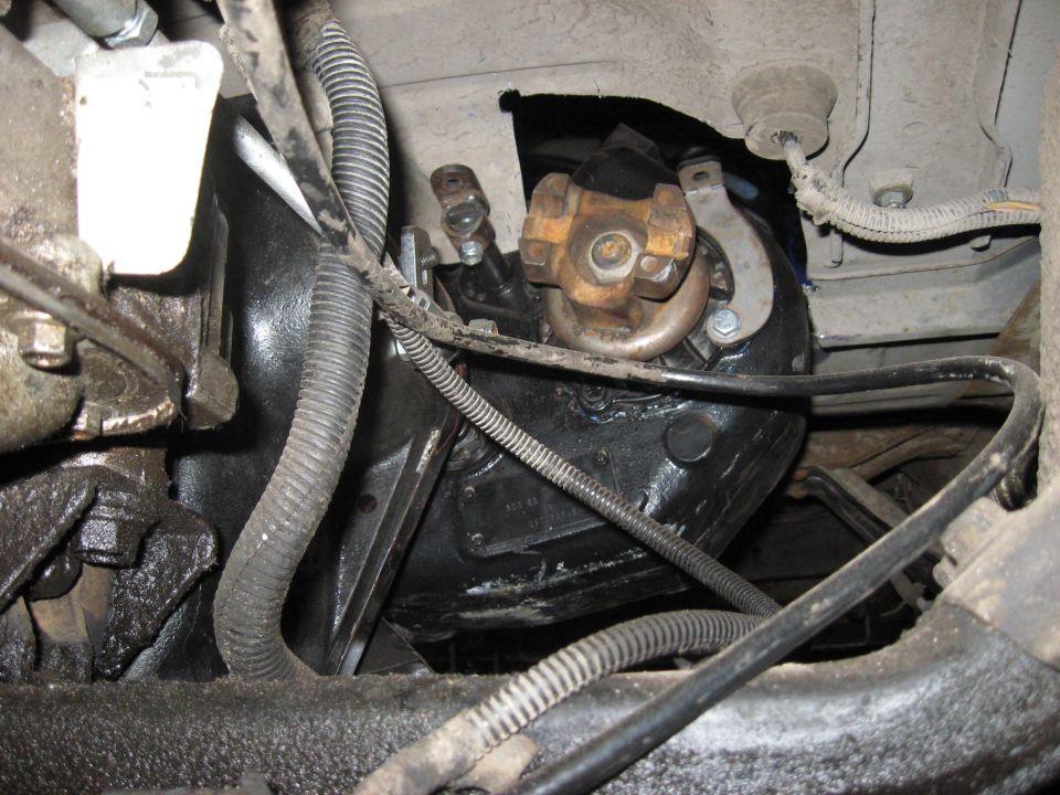 Underside view of vehicle's transmission housing, driveshaft U-joint, and associated wiring. Some oil residue is visible