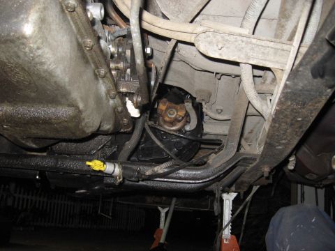 1991 Ford Bronco - Underside view of a vehicle's drivetrain, showing the transfer case and driveshaft, supported by jack stands.