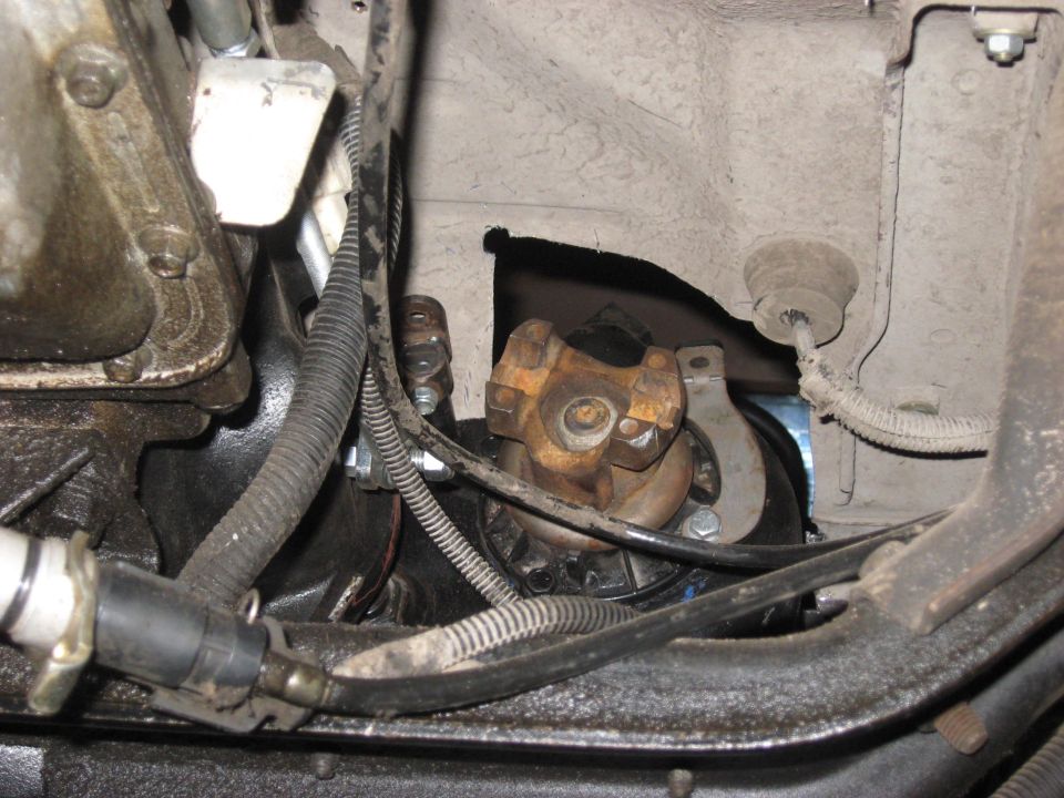 Close-up of a driveshaft U-joint and starter motor assembly, with wiring and engine components visible