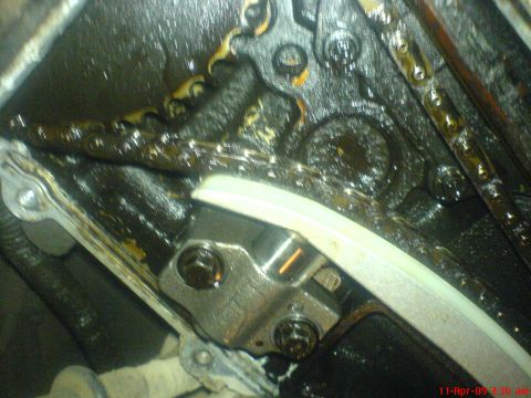 1992 Ford Crown Victoria - Close-up view of an engine's timing chain and tensioner, covered in oil.