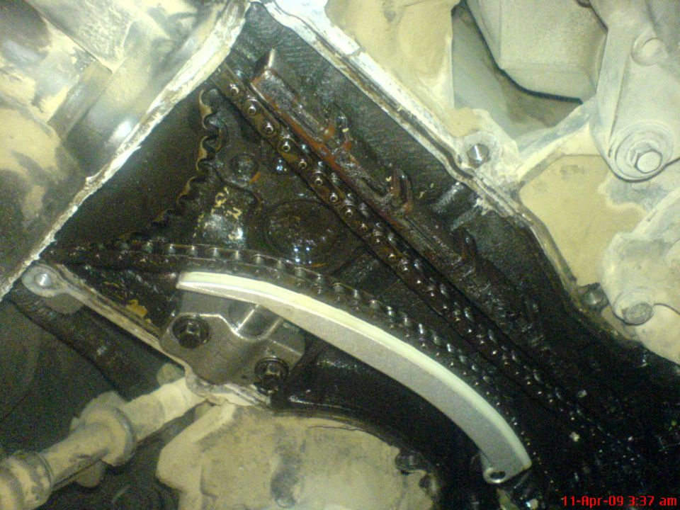 Engine timing chain and tensioner assembly with oil residue. Visible text: SUPERMOTORS.NET