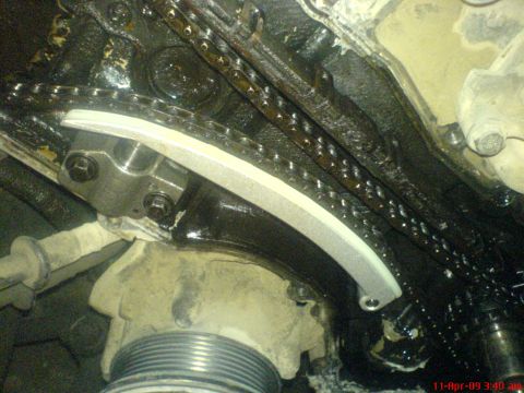 1992 Ford Crown Victoria - Close-up of an engine's timing chain and tensioner mechanism, covered in oil.