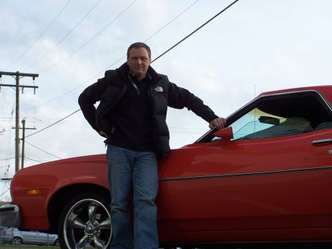 1973 Ford Ranchero - A man stands next to a red 1973 Ford Ranchero GT, with a utility bed visible.