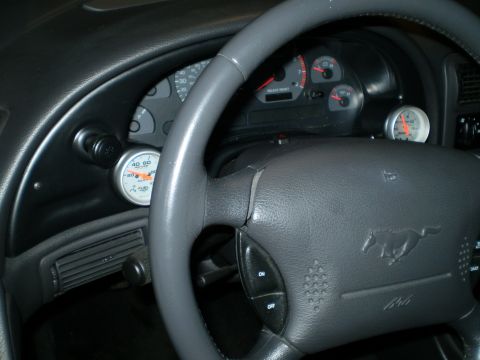 2002 Ford Mustang - The dashboard of a 2002 Ford Mustang features its iconic horse emblem on the steering wheel and several gauges, including an aftermarket, g…