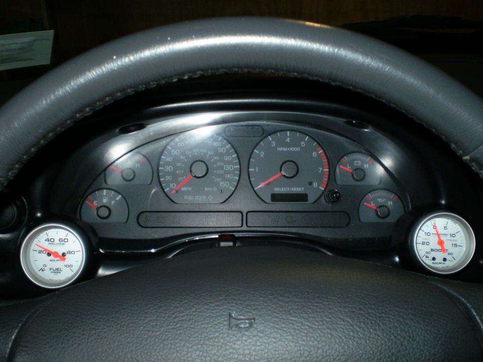 Car dashboard with speedometer, tachometer, fuel gauge, and two aftermarket gauges (boost and fuel pressure)
