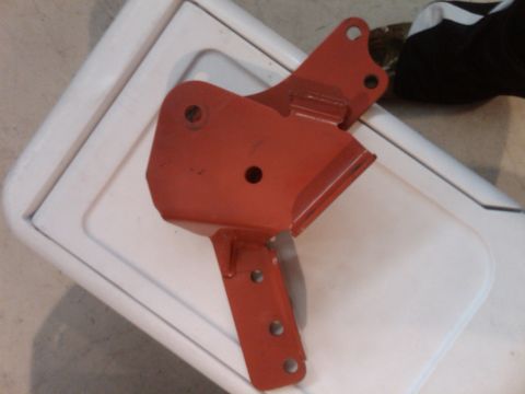 1982 Ford Bronco - A red metal bracket with several bolt holes is shown against a white surface.