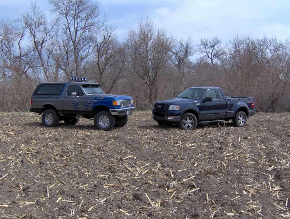Blue Ford F-150 pickup and a lifted blue Bronco parked in a field