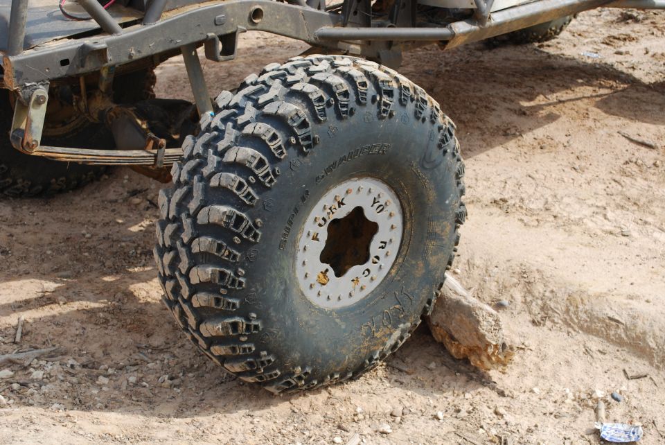 Close-up of a large off-road tire with 'FUCK ROCK YO' written on the rim. Suspension components are visible
