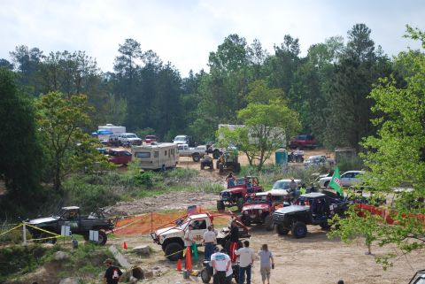 2008 Jeep Wrangler - Multiple off-road vehicles and recreational vehicles are parked in a dirt lot surrounded by trees.