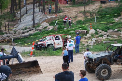 2008 Jeep Wrangler - Off-road trucks and spectators gather at an event with rocky terrain in the background.