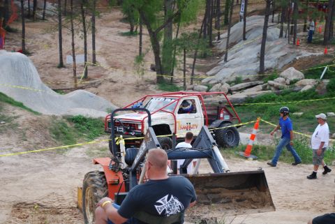 2008 Jeep Wrangler - A modified truck with a roll cage is at an off-road event, with a loader tractor nearby.