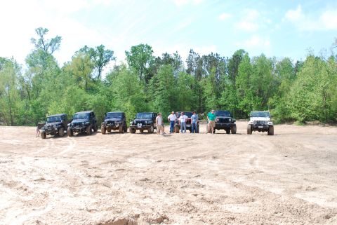 2008 Jeep Wrangler - A group of Jeep Wranglers are gathered on a sandy lot, with a line of trees visible in the background.